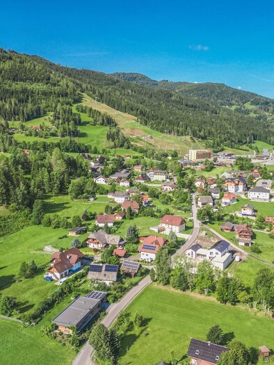 A picturesque landscape with green hills and a small village. The houses are surrounded by forests and meadows.