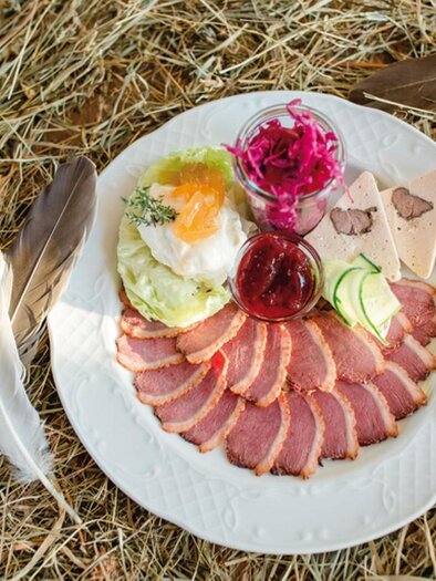 Ein Teller mit verschiedenen Fleischspezialitäten, Salat und Marmelade. Der Teller ist auf einem Bett aus Heu platziert. | © Buschenschank Tinnauer