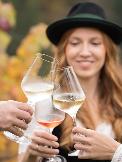 Ein Glas mit Wasser wird in der Hand gehalten. Im Hintergrund sind verschwommene Silhouetten von Menschen und eine entspannte Atmosphäre. | © Flora P. - Wein Steiermark