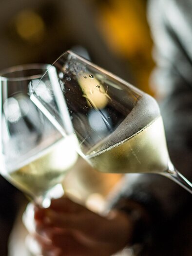 Zwei Gläser Sekt stoßen an. Im Hintergrund sind unscharfe Lichter zu sehen. | © TV Südsteiermark