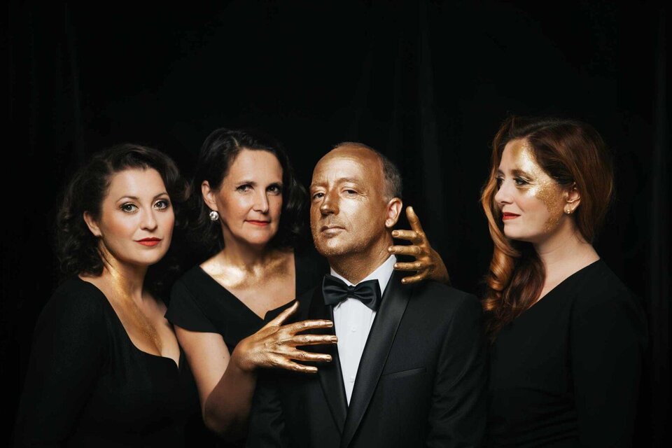 Zwei Frauen sitzen an einem Tisch und halten Sand in der Hand. Der Hintergrund ist neutral, und der Titel "PIANO & SAND" ist prominent platziert. | © KOMM.ST