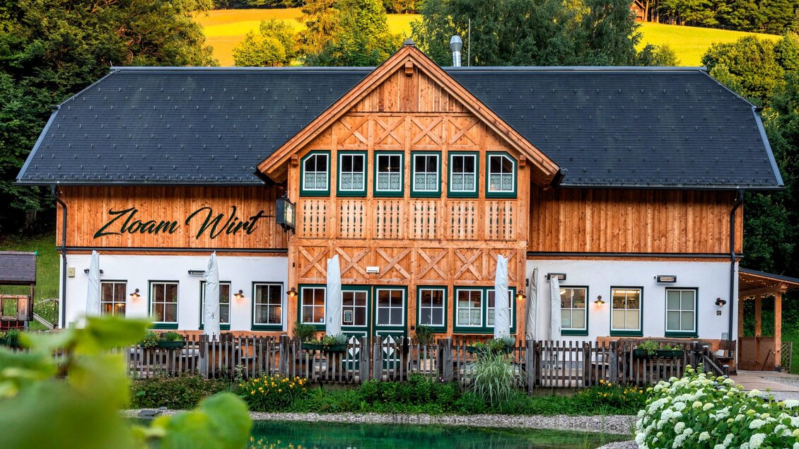 Ein charmantes Gasthaus mit Holzfassade und großen Fenstern. Es liegt an einem ruhigen Teich, umgeben von grünen Wäldern. | © www.zloamwirt.at