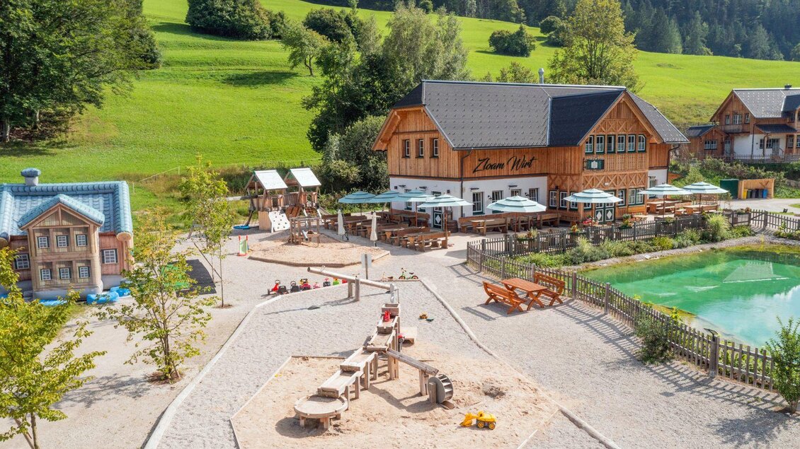 Eine einladende Anlage mit einem Spielplatz, einem Teich und mehreren Holzhäusern. Das große grüne Feld im Hintergrund schafft eine ruhige Atmosphäre. | © www.zloam.at