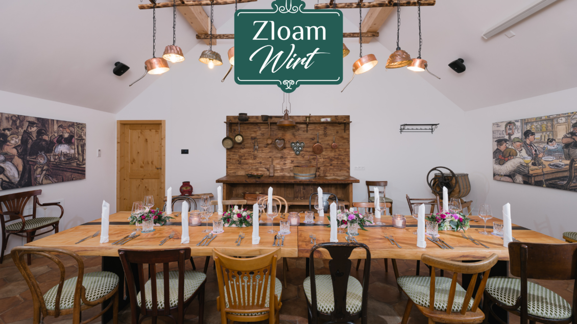 Ein einladender Tisch in einem gemütlichen Raum mit rustikalem Holzdekor und farbenfrohen Blumen. An den Wänden hängen zwei beeindruckende Bilder, die eine traditionelle Atmosphäre schaffen. | © Zloam Wirt, www.zloamwirt.at