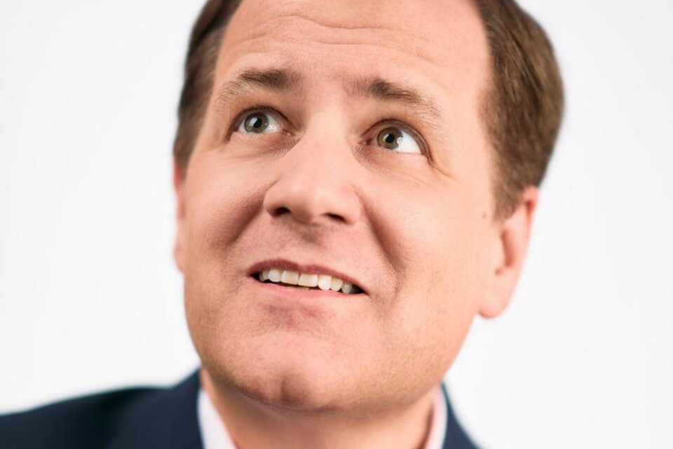 Ein Mann schaut optimistisch nach oben und lächelt. Er trägt einen dunklen Anzug mit einem hellen Hemd. | © Pressefoto Director's Cut! © Roman Pfeiffer
