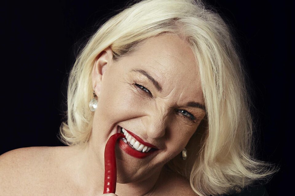 Eine Frau mit blonden Haaren lächelt verführerisch und hält eine kleine rote Peperoni. Sie trägt Schmuck und hat einen charmanten Gesichtsausdruck. | © Barbara Balldini