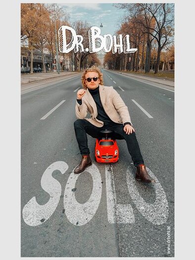 A young man is sitting on the street in a small red car. He is wearing sunglasses and looks relaxed. | ©  Dr. Bohl