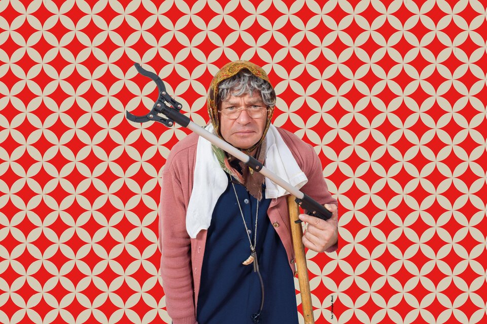 Eine ältere Frau mit Brille steht vor einem bunten, gemusterten Hintergrund. Sie hält einen Stock und trägt eine Kopfbedeckung. | ©  Christopher Marvic