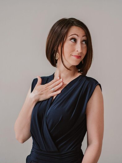 A woman in an elegant, dark blue dress looks curiously to the side. She has a confident expression and a hand-supported gesture. | © lynephptpgraphy