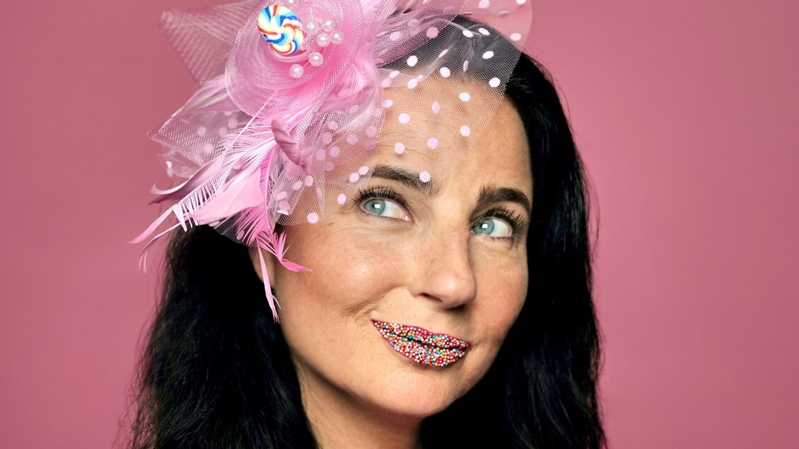 Kabarettistin Nadja Maleh mit rosa Kopfschmuck und bunten Zuckerperlen auf den Lippen vor rosa Hintergrund. | © Sabine Stieger