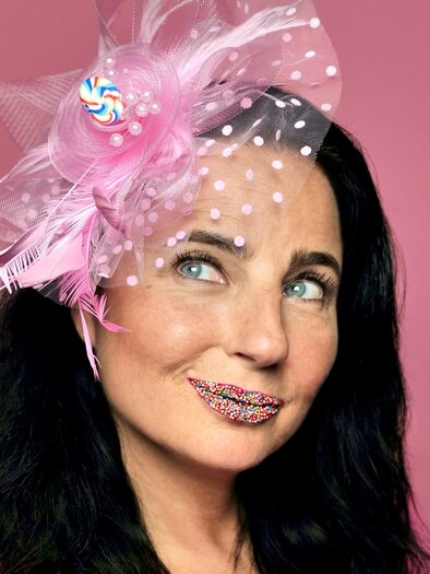 Cabaret artist Nadja Maleh with pink headgear and colorful sugar pearls on her lips against a pink background. | © Sabine Stieger
