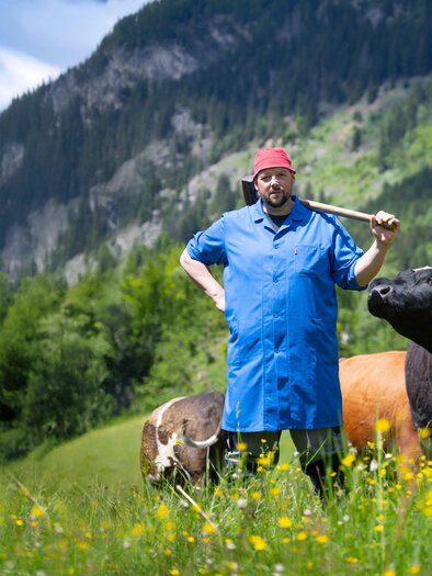 Petutschnig Hons with a red cap and hammer on a mountain meadow among cattle. | © Heimo Spindler