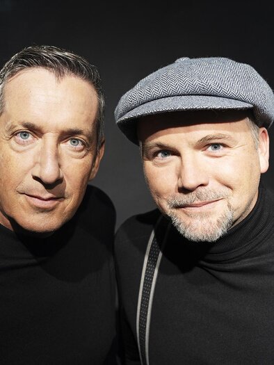Two men stand close together and look at the camera. They are wearing black tops, one has a gray cap on. | © Lukas Beck