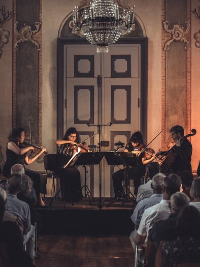 <p>Eine Streichergruppe mit vier Personen, spielt in einem sakalem Bauwerk bei mystischem List beim Kammer Musik Festival. </p> | © Reiter Media