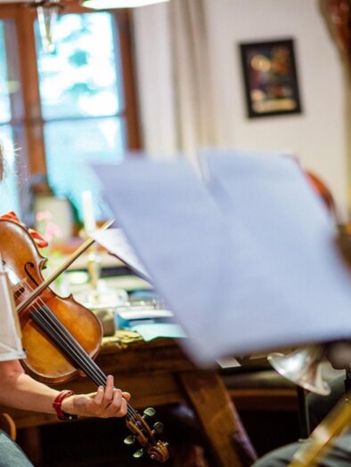 Musikerin Marie-Theres Härtel spielt die Violine während einer Probe mit ihrer Band im Rahmen des Kammer Musik Festivals in Edelschrott. Im Hintergrund sind weitere Musiker zu sehen, die verschiedene Instrumente wie Saxophon und Posaune spielen. | © Christoph Huber