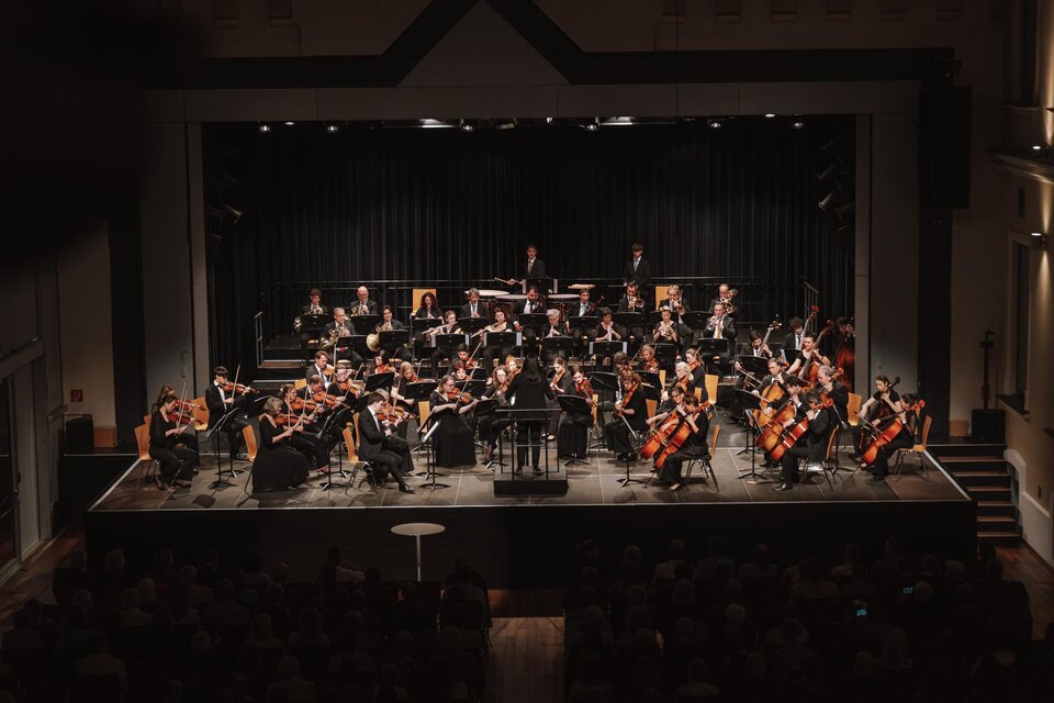 Man sieht die beeindruckende Größe des Gleisdorfer Kammerorchesters unter der Leitung von Frau Yu-Hao Lorenz, die als Dirigentin in der Mitte steht, vor den über fünfzig elegant in Schwarz gekleideten Musikerinnen und Musikern, mit den verschiedenen Instrumenten - von Geigen und Cellos bis hin zu Querflöten, Trompeten und anderen Blasinstrumenten sowie Percussionsinstrumenten im Hintergrund. | © Oststeiermark Tourismus