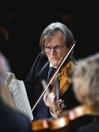 Ein älterer Mann spielt Violine auf einer Bühne. Er trägt einen Anzug und konzentriert sich auf die Musik. | © Ernst Friessnegg