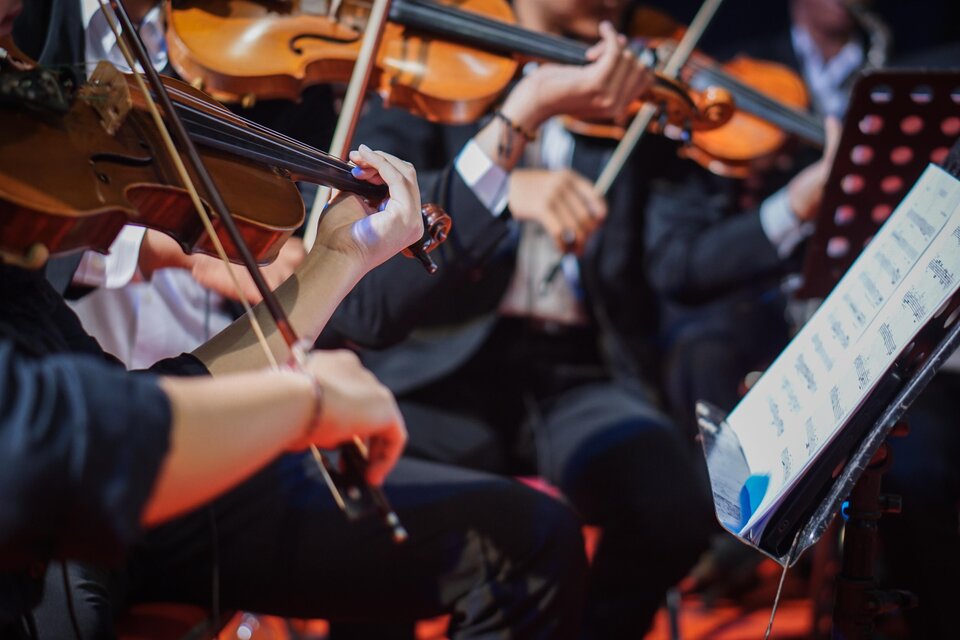 Ein Orchester spielt auf der Bühne. Man sieht Hände von Musikern, die Geigen halten und Notenblätter konsultieren. | © istock