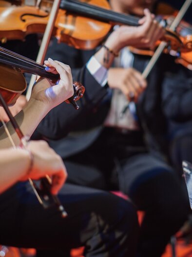 Ein Orchester spielt auf der Bühne. Man sieht Hände von Musikern, die Geigen halten und Notenblätter konsultieren. | © istock