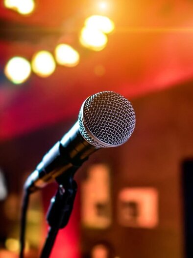 A microphone stands in the foreground against a blurred backlight. It signals a musical or social atmosphere. | © Pixabay