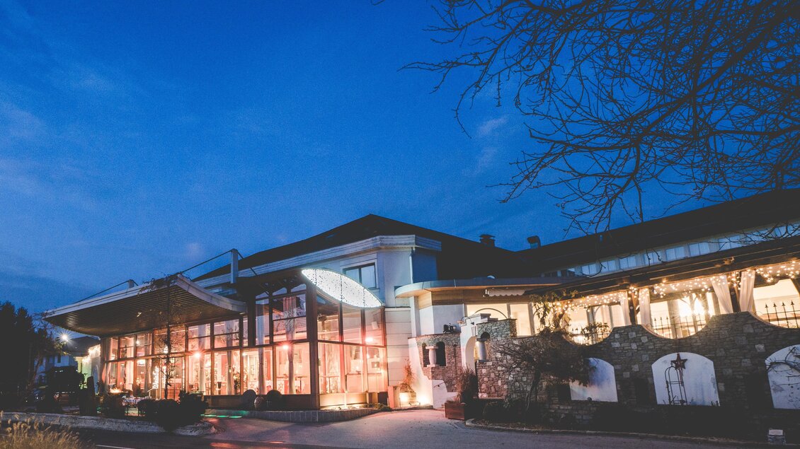 Ein modernes Gebäude bei Dämmerung, beleuchtet und einladend. Fensterfronten bieten einen Blick auf den Innenraum und die umgebende Natur. | © Garten Hotel Ochensberger