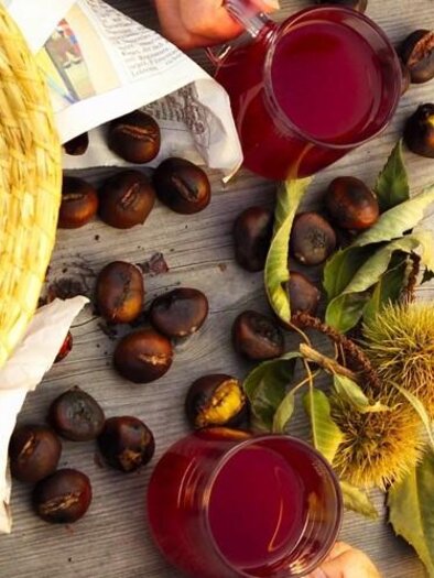 Roasted chestnuts, grapes, and a glass of red juice on a wooden board. The colors are warm and inviting. | © © Werner Krug