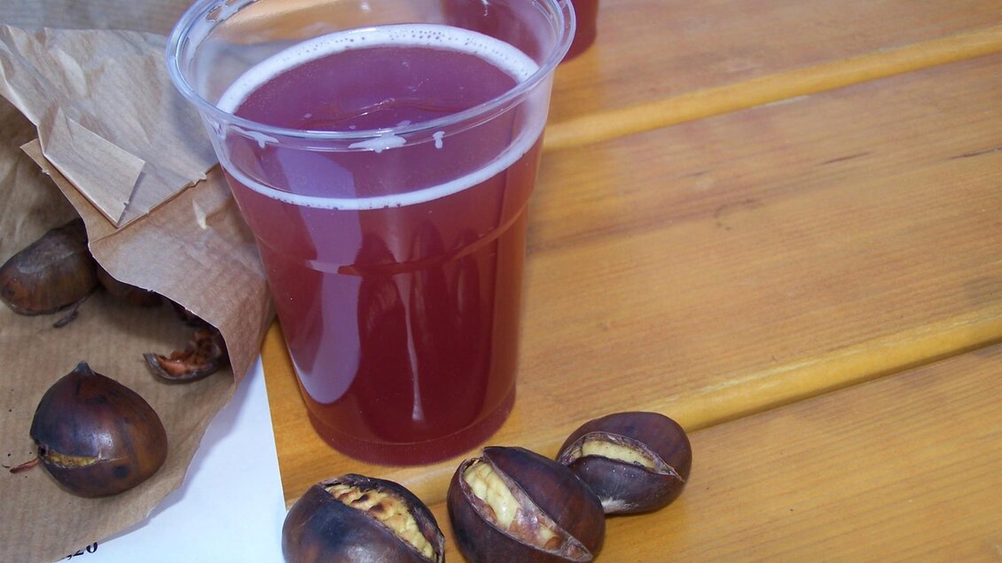 Ein Glas roter Saft steht auf einem Tisch aus Holz, daneben liegen geröstete Kastanien. Die Szene vermittelt eine gemütliche, herbstliche Atmosphäre. | © TV Thermen- & Vulkanland
