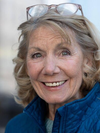 A photo of Erika Deutinger, who is presenting the recitation of the portrait of Katia Mann that evening. She is smiling and wearing a blue jacket, has a positive aura, and looks kindly at the camera. | © Erika Deutinger