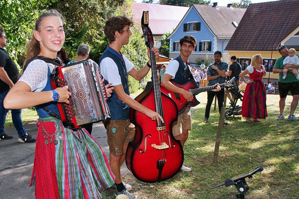Eine Gruppe junger Musiker spielt traditionelle Instrumente im Freien. Im Hintergrund sind Menschen bei einer Veranstaltung zu sehen. | © Helmut Adelwöhrer