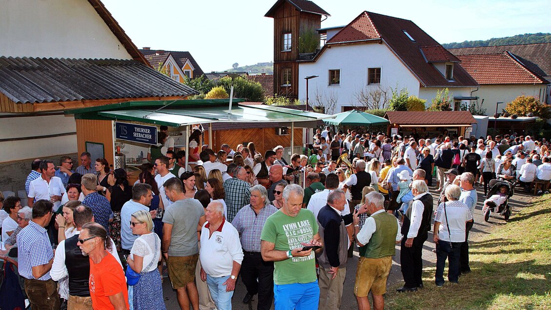 Eine große Menschenmenge versammelt sich vor einem lokalen Fest. Alte und neue Gebäude umgeben die fröhliche Atmosphäre im Freien. | © Helmut Adelwöhrer