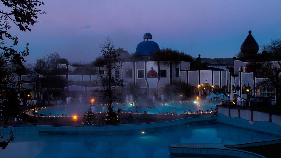 Ein entspannendes Thermalbad bei Dämmerung, umgeben von stimmungsvollem Licht. Der Pool dampft sanft und lädt zum Relaxen ein. | © Hundertwasser Architekturprojekt