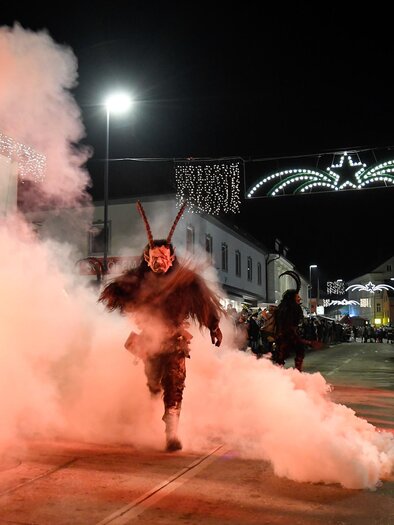 Eine Person läuft durch eine rauchige Straße bei Nacht. Im Hintergrund sind Lichter und Verkaufsstände zu sehen. | © Stadtgemeinde Kindberg