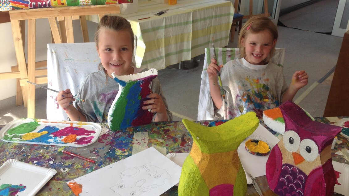 Zwei Kinder sitzen an einem Tisch und malen farbenfrohe Figuren. Der Tisch ist mit Malutensilien und bunten Kunstwerken bedeckt. | © Marlene Schaumbeger
