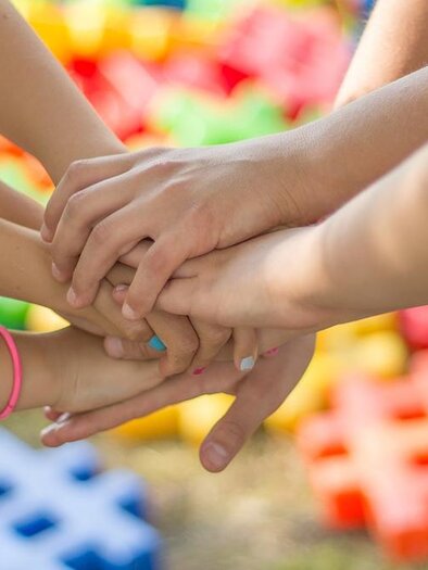 Viele Hände sind übereinander geschichtet, die Zusammenarbeit symbolisierend. Im Hintergrund sind bunte Spielsteine sichtbar. | © Bild: Pixabay