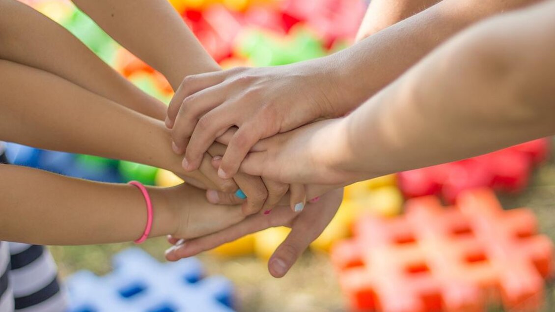 Hände von verschiedenen Personen, die übereinander gestapelt sind. Im Hintergrund sind bunte Spielzeugplatten zu sehen. | © Bild: Pixabay
