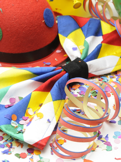 Various carnival items such as a brightly patterned bowtie and a red hat, decorated with colorful streamers and colorful confetti on a white background. | © Canva