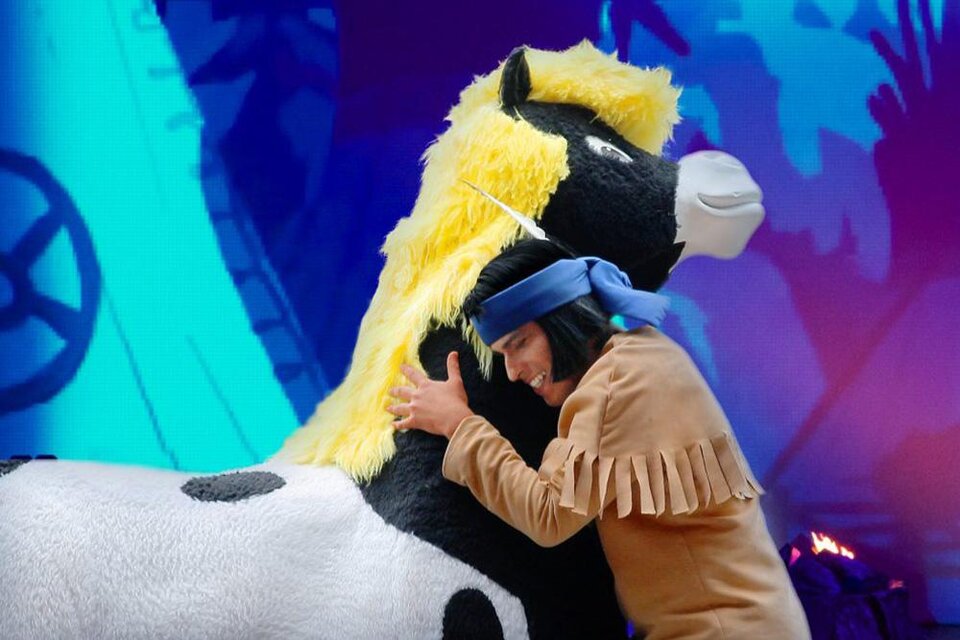 Ein Mensch umarmt ein großes, plüschiges Pferd mit einer gelben Mähne. Der Hintergrund ist bunt und fröhlich gestaltet. | © Bild: Theater mit Horizont