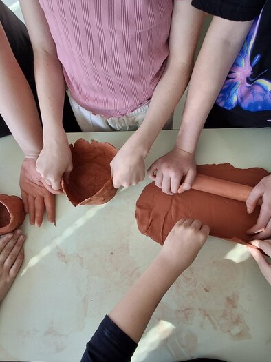 Eine Gruppe von Menschen arbeitet mit Ton auf einem Tisch. Ihre Hände formen verschiedene Objekte aus dem Material. | © Vesna Vesel