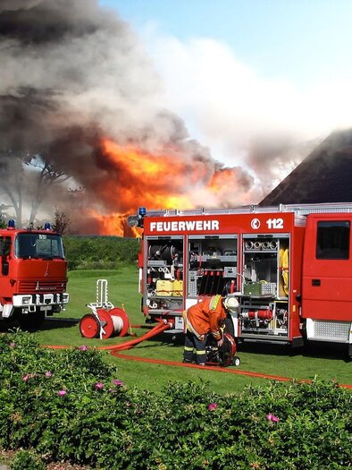 Ein Feuerwehrauto steht bereit, während im Hintergrund ein großes Feuer brennt. Feuerwehrmänner sind aktiv mit der Brandbekämpfung beschäftigt. | © pixabay
