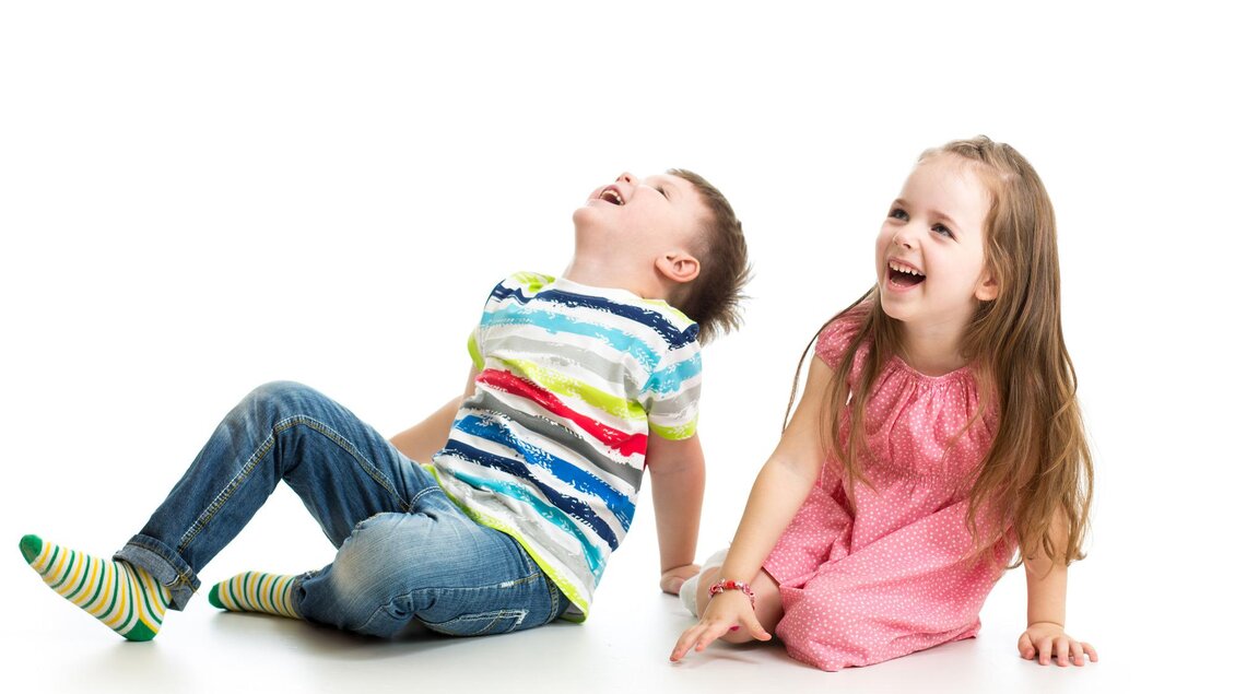 Zwei Kinder lachen und sitzen auf dem Boden. Das Mädchen trägt ein pinkes Kleid und der Junge ein gestreiftes T-Shirt. | © TV Südsteiermark - Adobe Stock