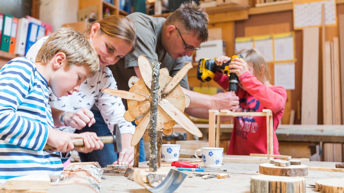 Eine Familie arbeitet gemeinsam an handwerklichen Projekten in einer Werkstatt. Kinder und Erwachsene verwenden verschiedene Werkzeuge, um kreative Holzarbeiten zu erstellen. | © Dominik Steiner