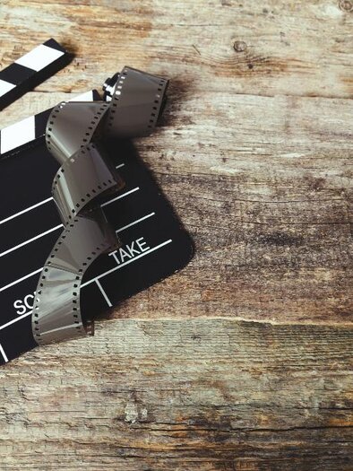 Ein Filmklappengerät liegt auf einem Holzuntergrund. Daneben sind Filmstreifen sichtbar. | © Bild: freepik