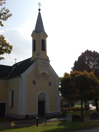 Eine kleine gelbe Kirche mit einem spitzen Turm. Umgeben von Bäumen und einem ruhigen Dorf. | © Stadtgemeinde Fehring