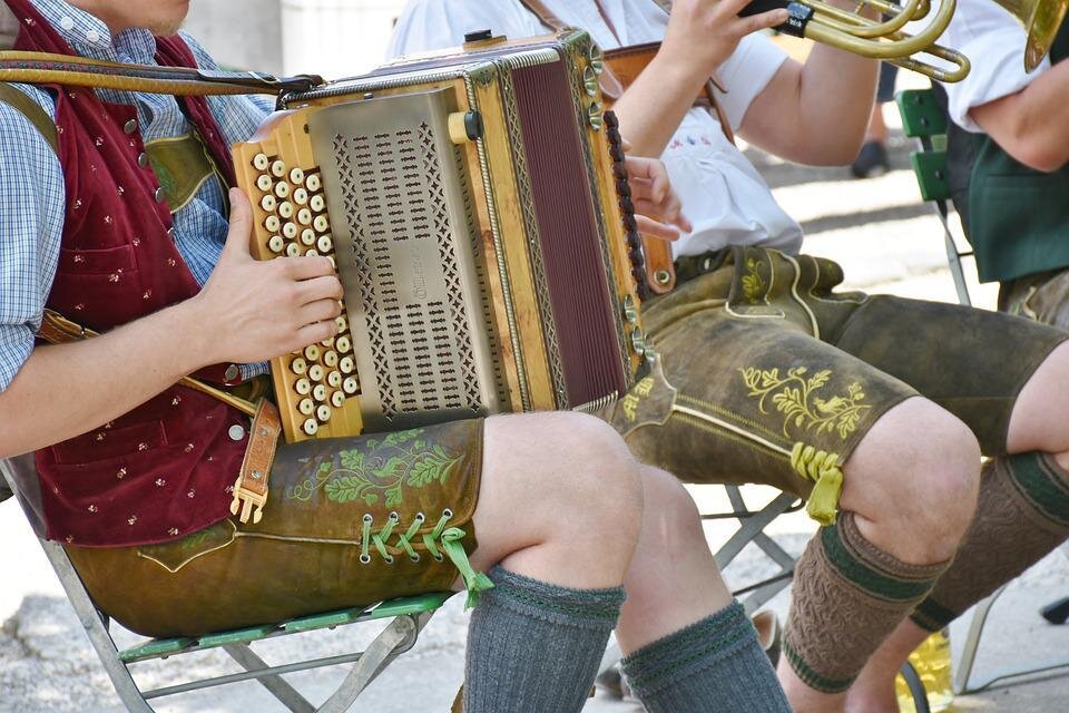 Eine traditionelle bayerische Musikgruppe spielt auf einer Straße. Man sieht detailreiche Trachten und ein Akkordeon. | © Pixabay