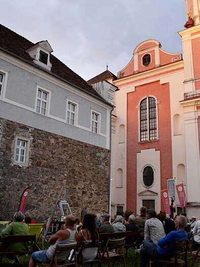 Ein Freiluftkino mit einem großen Bildschirm und Menschen, die Filme schauen. Im Hintergrund ist ein historisches Gebäude mit einer schönen Fassade zu sehen. | © Peter Brandl-Rupprich