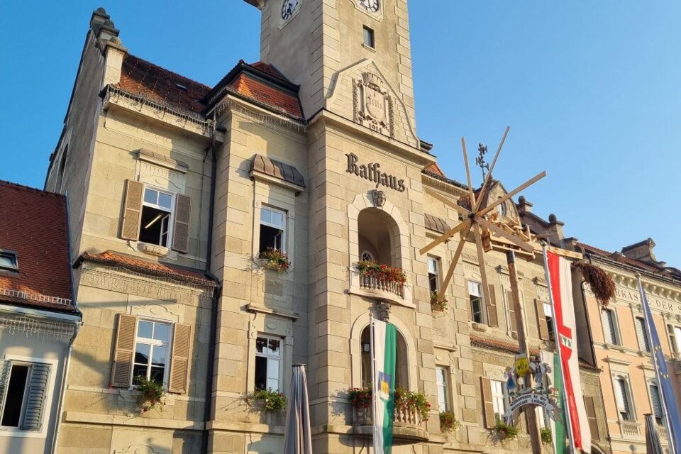 Eine malerische Stadtansicht mit historischen Gebäuden und einem auffälligen Windrad im Vordergrund. Der Himmel ist klar und blau, was eine entspannte Atmosphäre schafft. | © @Andrea Kölbl