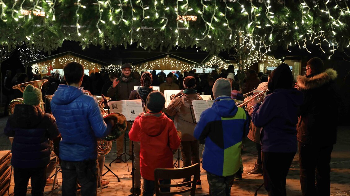 Eine Gruppe von Musikern spielt in einer festlich beleuchteten Umgebung. Um sie herum stehen Menschen in warmen Kleidern und genießen die Atmosphäre. | © Foto de Monte Mureck