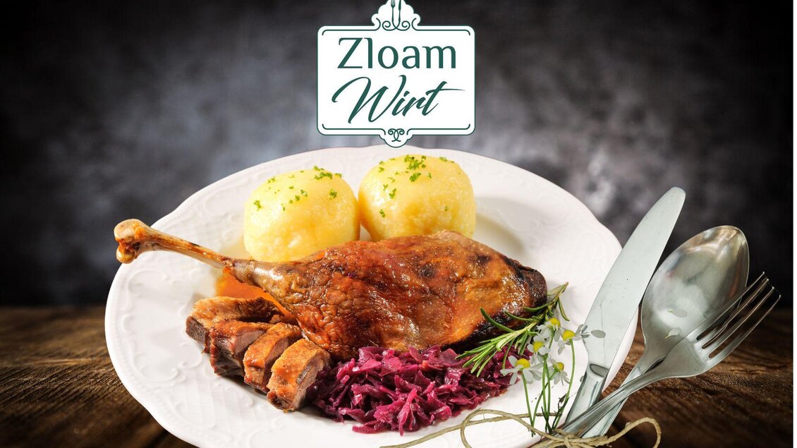 Ein köstlicher Teller mit gebratener Ente, Rotkohl und Kartoffelknödeln. Im Hintergrund ist das Logo "Zloam Wirt" sichtbar. | © www.zloam.at
