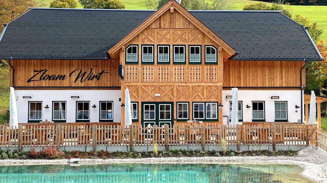 Ein charmantes Holzhaus mit einem eleganten Design, umgeben von grünen Wiesen. Vor dem Gebäude befindet sich ein klarer Wassersee.