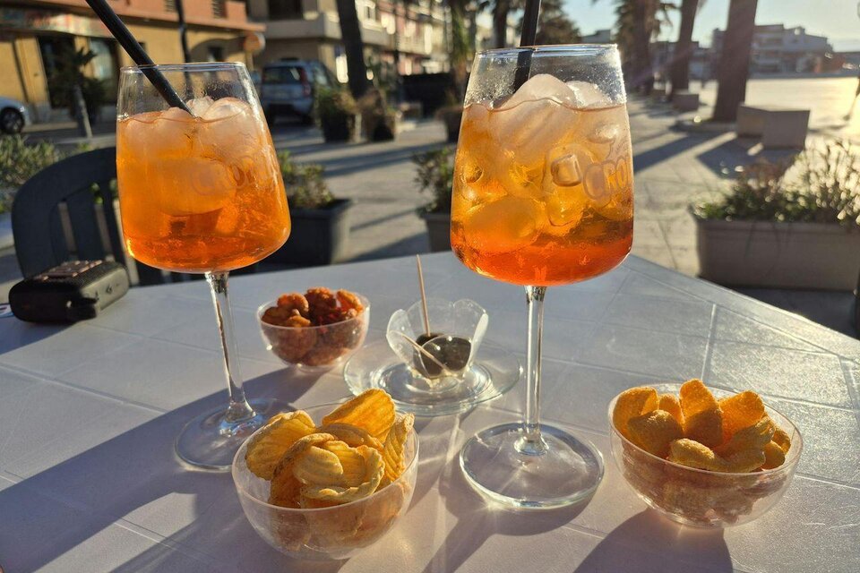 Zwei Gläser mit orangefarbenen Cocktails und Eiswürfeln stehen auf einem Tisch. Nebenbei sind verschiedene Snacks in kleinen Schalen angeordnet. | © AndersOrt Haus der Frauen
